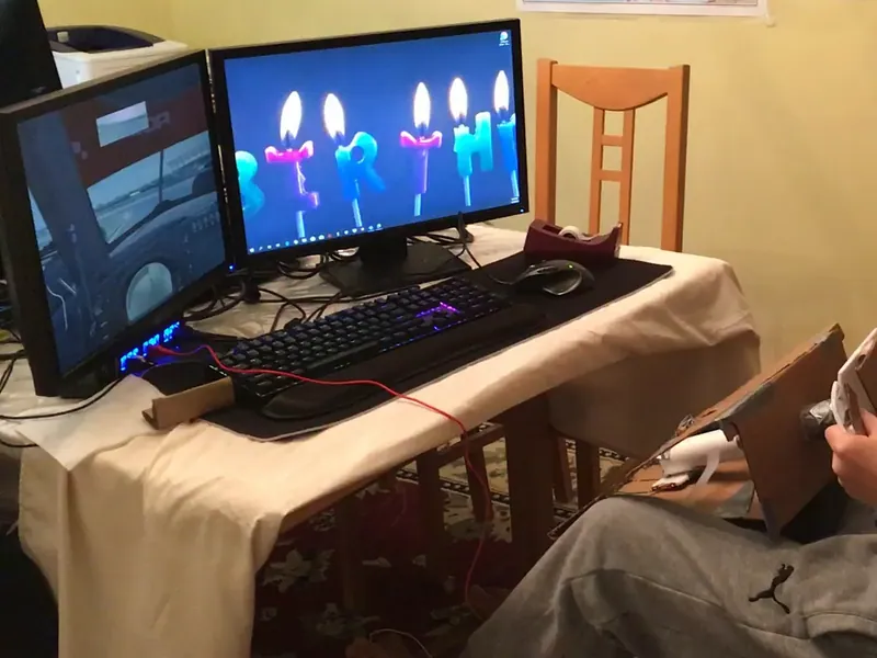 Day one: the cardboard wheel on its slanted stand in the driver's lap, the race on the left monitor (cropped to the simulator)