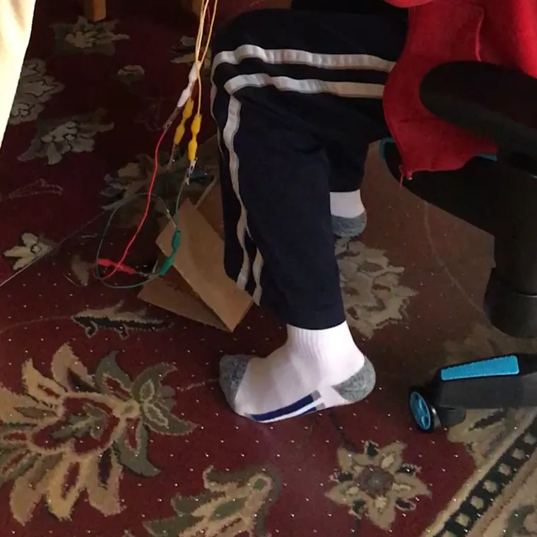 A cardboard pedal on the floor, with the clip leads running down to it from the desk