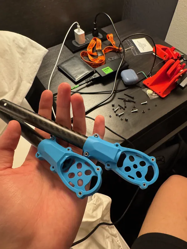 Spare carbon drone arms with their blue motor mounts, and red printed claw parts behind