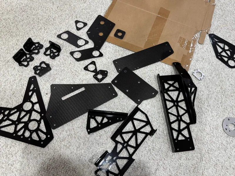 The custom parts laid out: carbon fiber plates and black powder-coated aluminum lattice parts