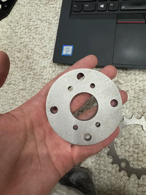 The stainless adapter plate that couples the keyed hub to the chain sprocket, with the sprocket behind it