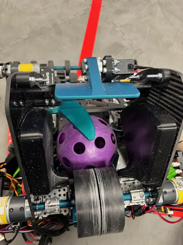 From behind: a ball waits under the teal gate, just past the flywheel pair