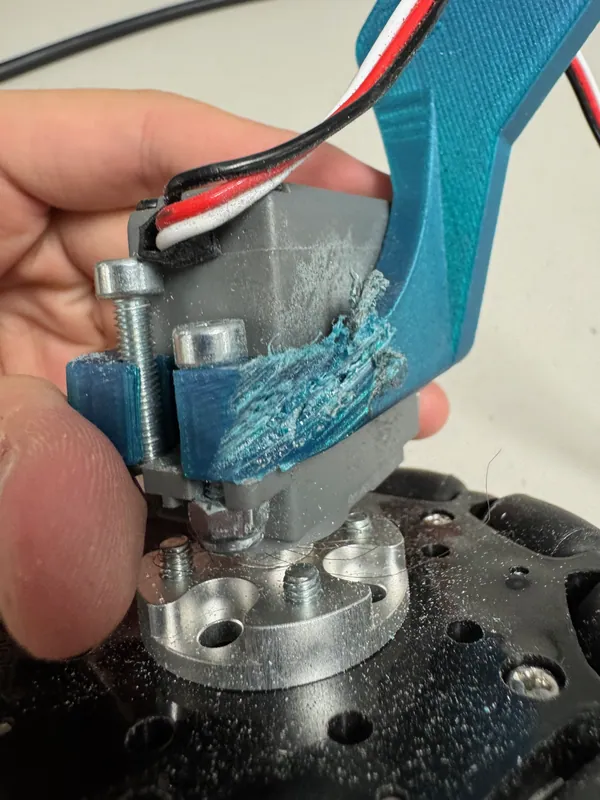 April 13, during the V2 build: an earlier printed servo mount, torn open along its layers at a screw
