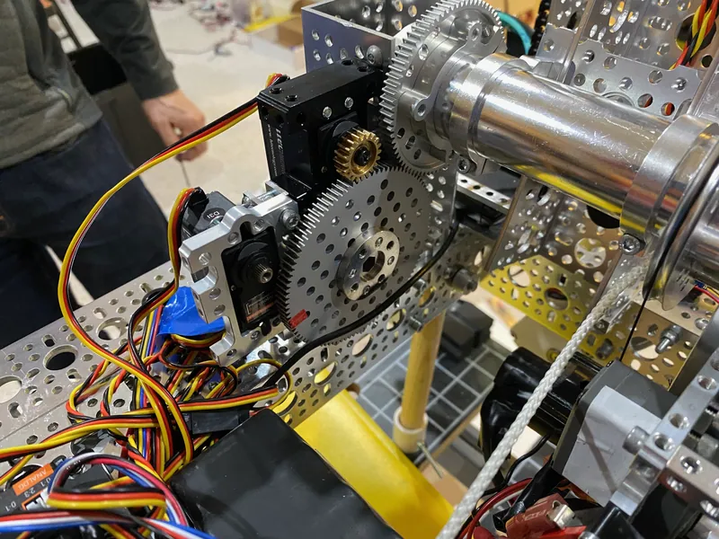 Feb 8, 2023, at the base of the arm: a servo with a brass pinion meshing with a large aluminum gear