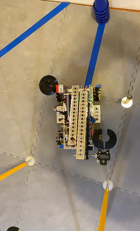 January 31, 2023, from above: the arm folded along the chassis, the claw open at one end, and a stack of cones against the wall