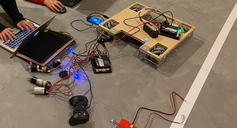 Day 10: loose motors and servos wired up on the field floor, with a laptop and a gamepad